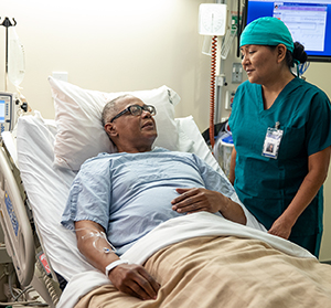 Health care provider talking to man in hospital bed.