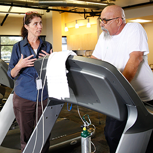 Healthcare provider coaching man walking on treadmill wearing nasal cannula.