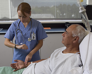 Healthcare provider checking man's pulse in hospital bed.